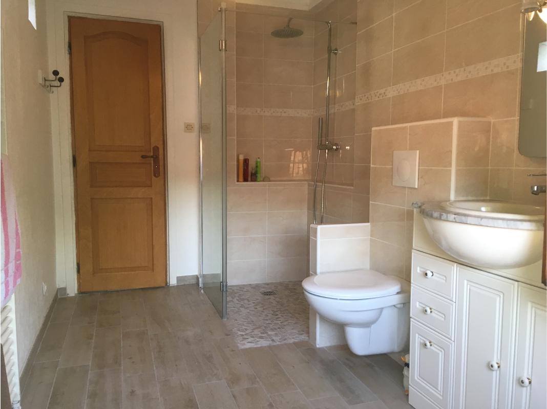 Salle de bain classique avec du carrelage beige, des wc suspsendy et un pommeau en hauteur.